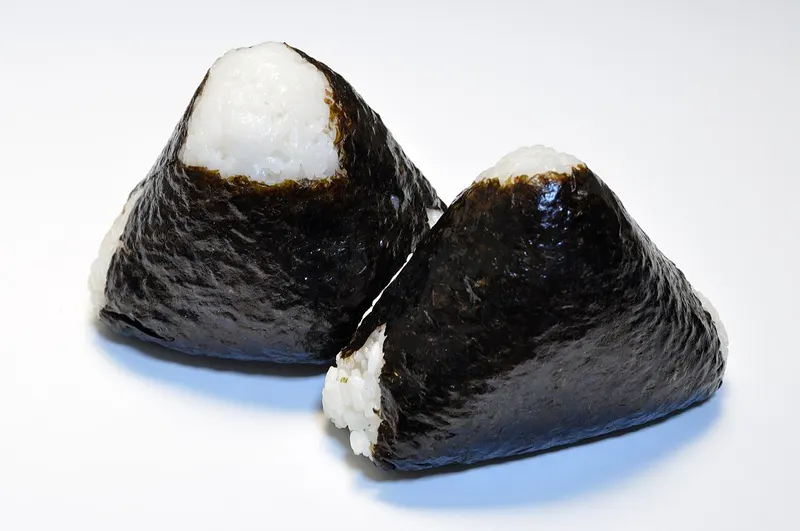 Dos onigiris triangulares con alga sobre fondo blanco