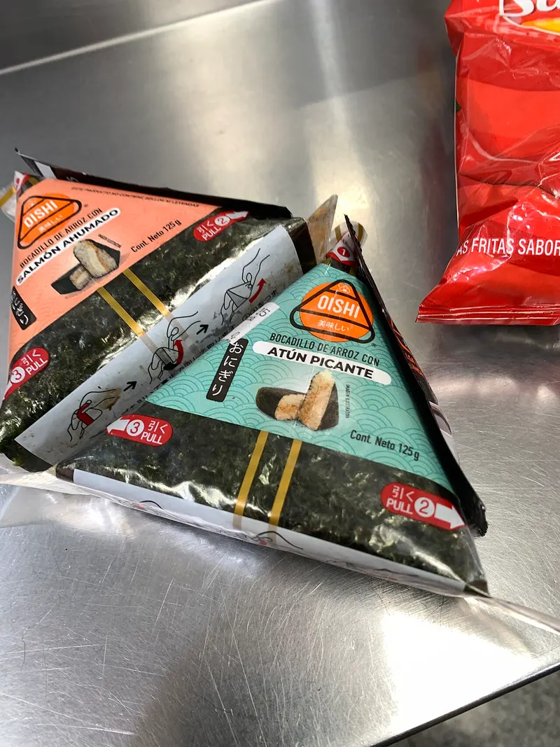 Dos onigiris envueltos en alga y plástico, uno de atún picante